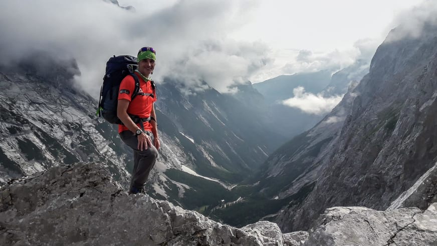 Auf hellem Kalksteinfels sitzt Bergwanderführer Markus Arndt mit roter Outdoorjacke und Blick ins tiefe Tal.