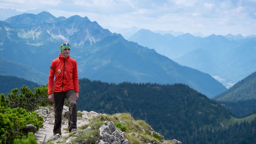 Bergwanderführer Markus Arndt in roter Softshelljacke steht auf steinigem Berggrat mit weiter Berglandschaft.