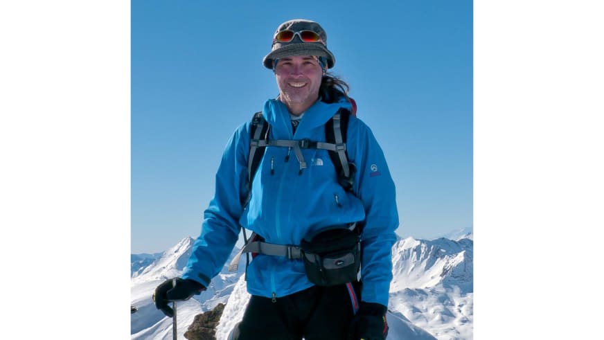 Bergwanderführer Markus Arndt in blauer Winterjacke und grauem Sonnenhut vor schneebedeckten Gipfeln.