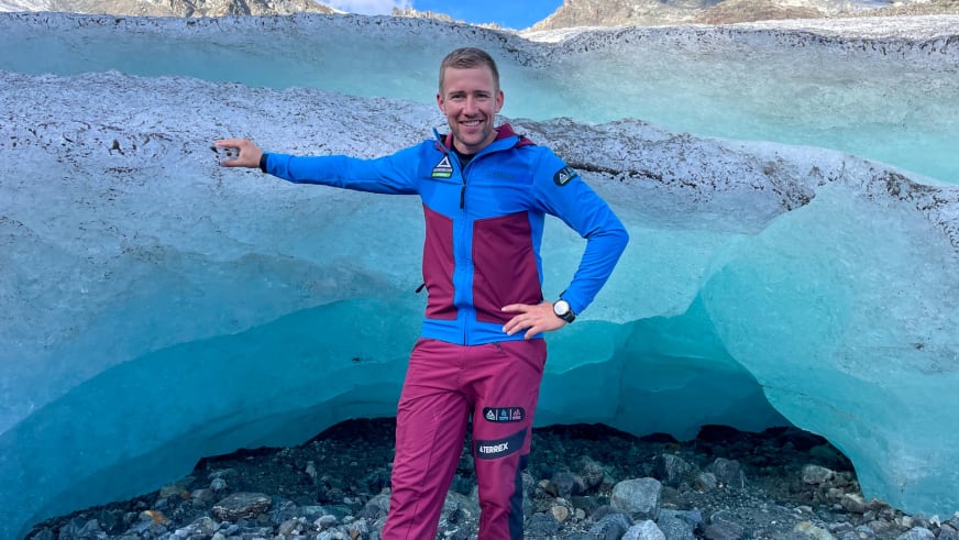 Bergführer Julian Conrad steht in blau-roter Outdoor-Bekleidung präsentierend vor einer Gletscherspalte mit türkisblauen Eiswänden.
