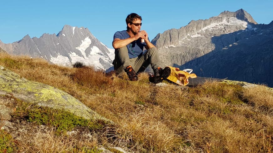 Bergführer Georg Schwarzenberger macht Pause auf grasigem Berghang mit gelbem Rucksack und trinkt aus einer Flasche.