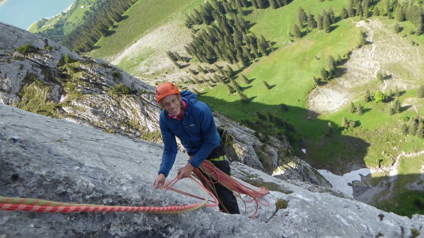 Bergführer Florian Lorenz klettert mit orangem Helm und blauer Jacke an einer steilen Kalksteinwand der Watzmann Ostwand.