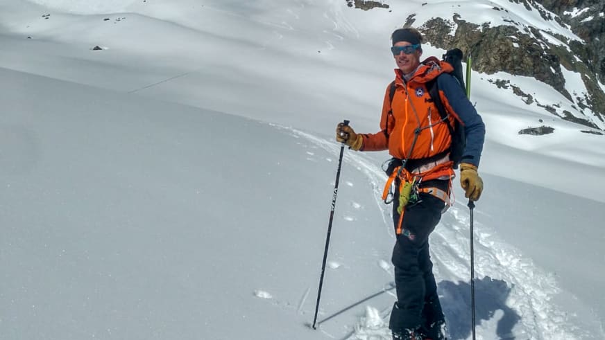Im tiefen Pulverschnee steht Bergführer Florian Lorenz mit orange Hardshell-Jacke und zwei Skistöckern auf einem Gletscherhang.