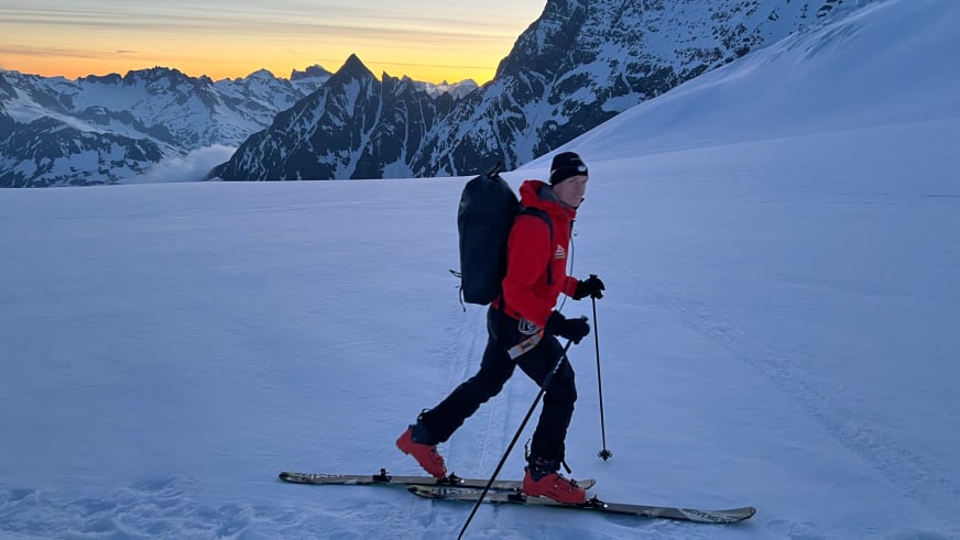 Bergführer Florian Lorenz bewegt sich auf Tourenskiern über einen schneebedeckten Gletscher in roter Jacke bei warmer Abendstimmung.