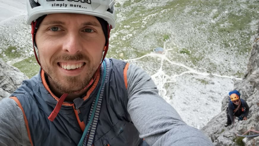 Am hellen Kalkstein lächelt Bergführer Paul Lohse mit weißem Helm und bunten Kletterseilen um den Hals in die Kamera.