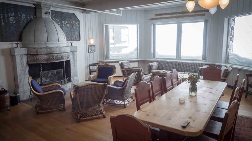 Gastraum im Hotel Finse 1222 mit steinernem Kamin und Holztisch für Gruppen unter weißen Holzbalken.