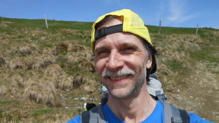 Bergwanderführer Thomas Schill trägt gelbes Käppi und Stirnlampe, dahinter hügelige Landschaft mit grünen Wiesen.