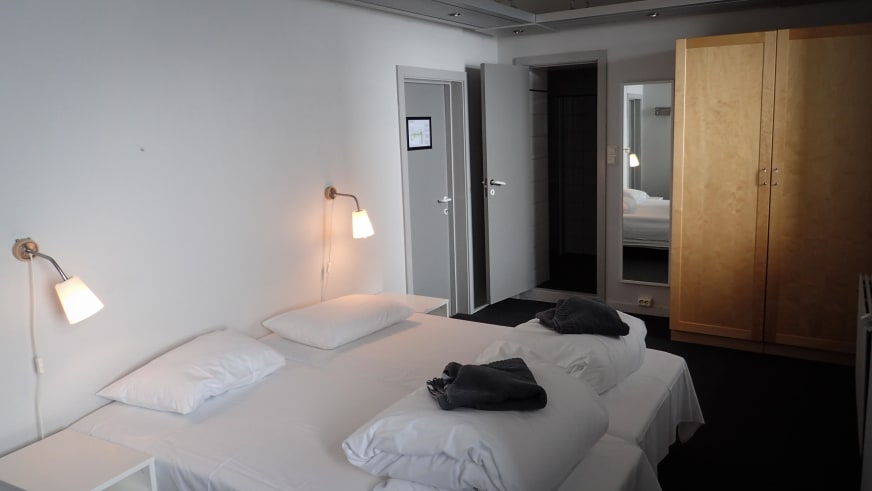 Modernes Hotelzimmer mit zwei Einzelbetten und hellem Kleiderschrank im Hotel Finse 1222 mit Wandleuchten.