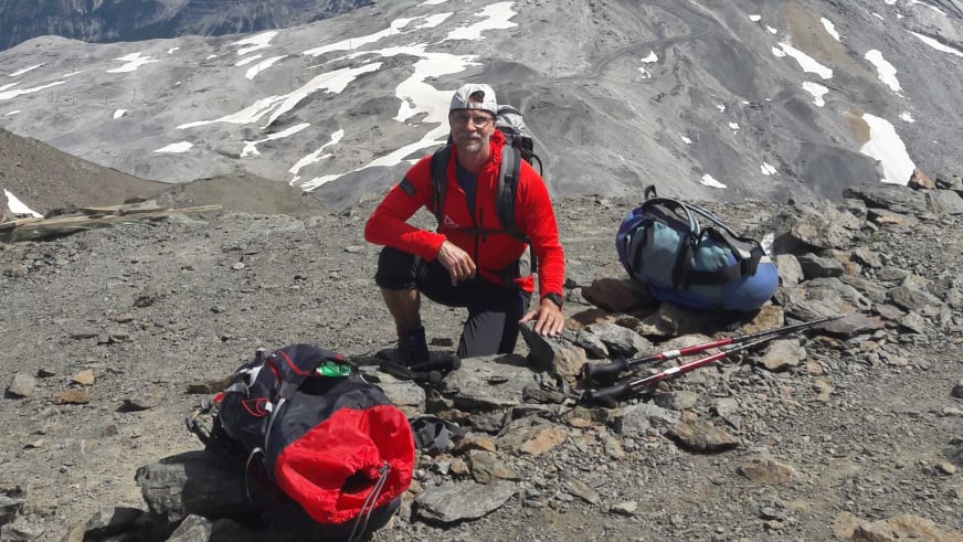 Bergwanderführer Thomas Schill hockt lächelnd zwischen ausgebreiteten Rucksäcken und Wanderausrüstung im Hochgebirge.