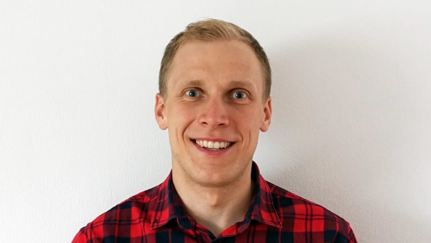 Bergführer Jan Schneider lächelt vor weißer Wand und trägt ein rot-schwarz kariertes Hemd mit Kragen.