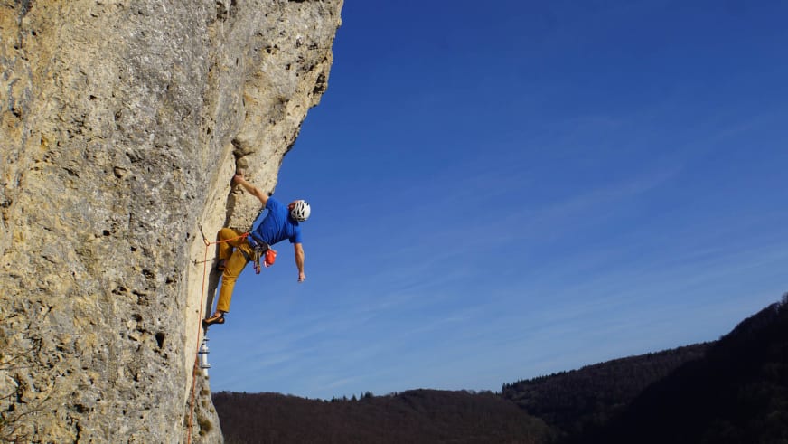 In blauem Shirt und weißem Helm klettert Bergführer Jan Schneider an löchriger Kalksteinwand in den Dolomiten.