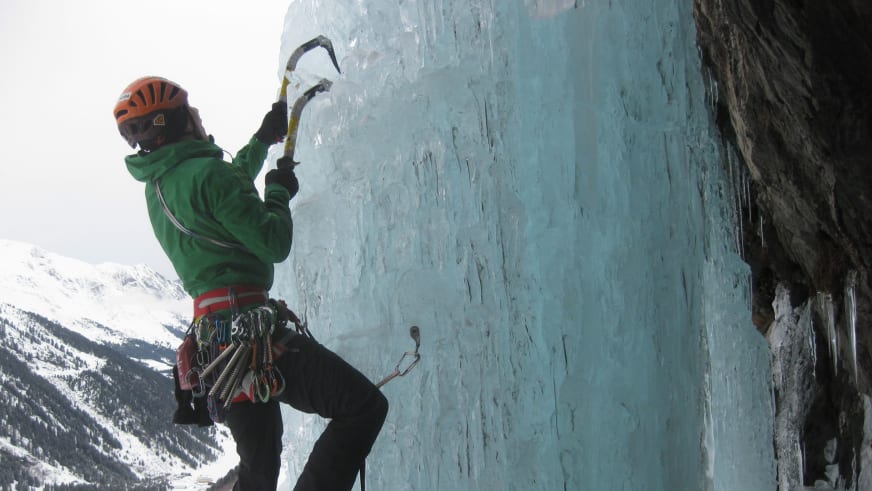 An einer bläulichen Eiswand klettert Bergführer Jan Schneider mit grüner Jacke und orangem Helm.