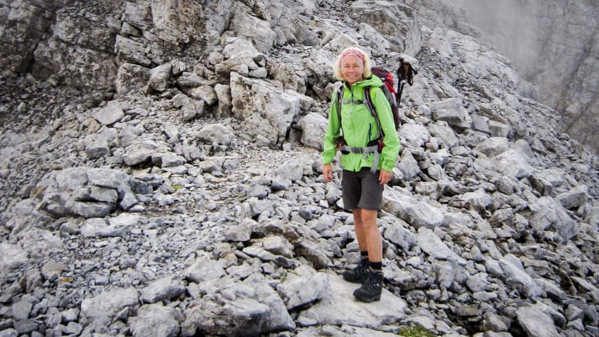Bergwanderführerin Friedlinde Hillmann steht lächelnd zwischen Kalksteinblöcken in grüner Softshelljacke und rotem Rucksack.