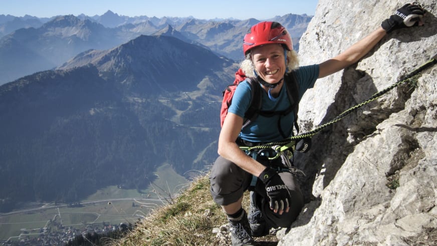 Bergwanderführerin Friedlinde Hillmann klettert mit Klettergurt und rotem Helm an steiler Kalksteinwand über dem Tal.