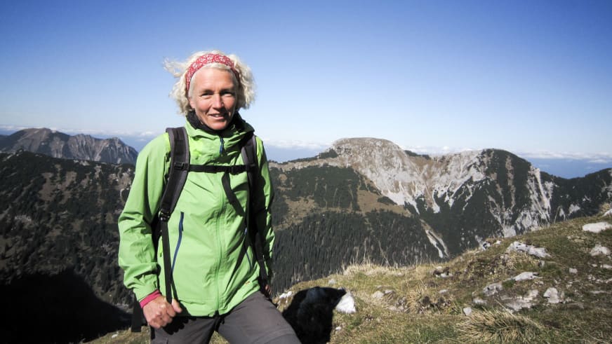 Auf einem Berggipfel lächelt Bergwanderführerin Friedlinde Hillmann in hellgrüner Jacke vor weitem Bergpanorama.