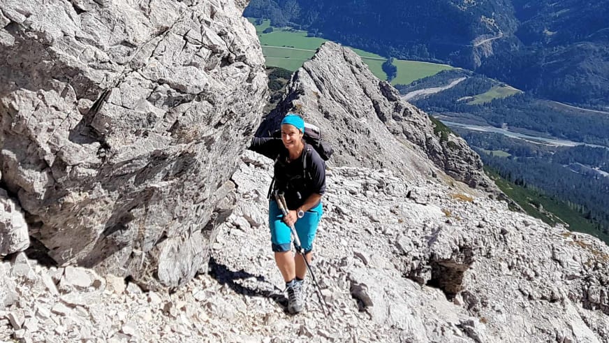 Bergwanderführerin Sabine Kühl mit türkisem Stirnband steigt über hellen Kalksteinschutt an einem steilen Felshang auf.