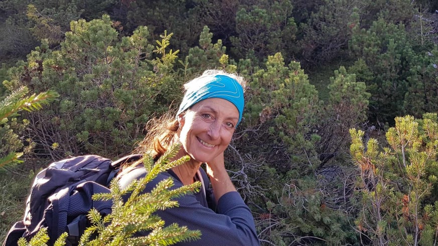 Lächelnde Bergwanderführerin Sabine Kühl mit blauem Stirnband vor Nadelwald in Südtirol.