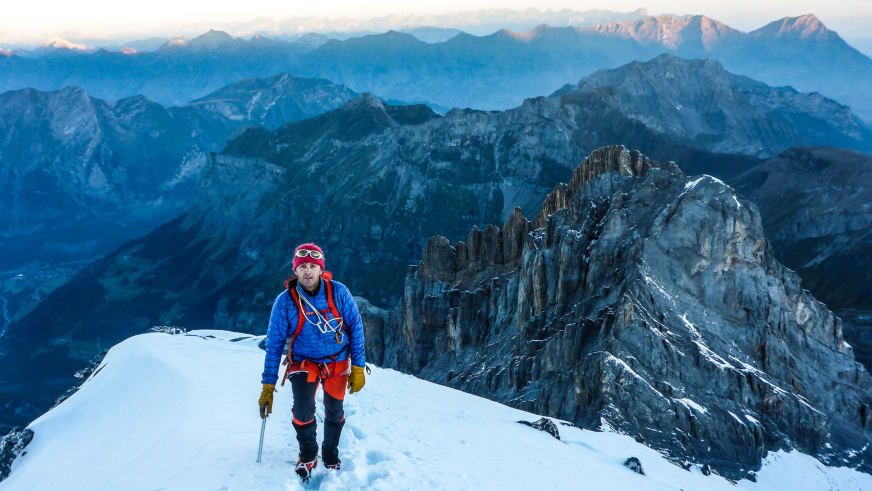 Auf einem schmalen Firnkamm am Ortler steht Bergführer Markus Hofmann mit Seil und Bergstock bei Morgenstimmung.