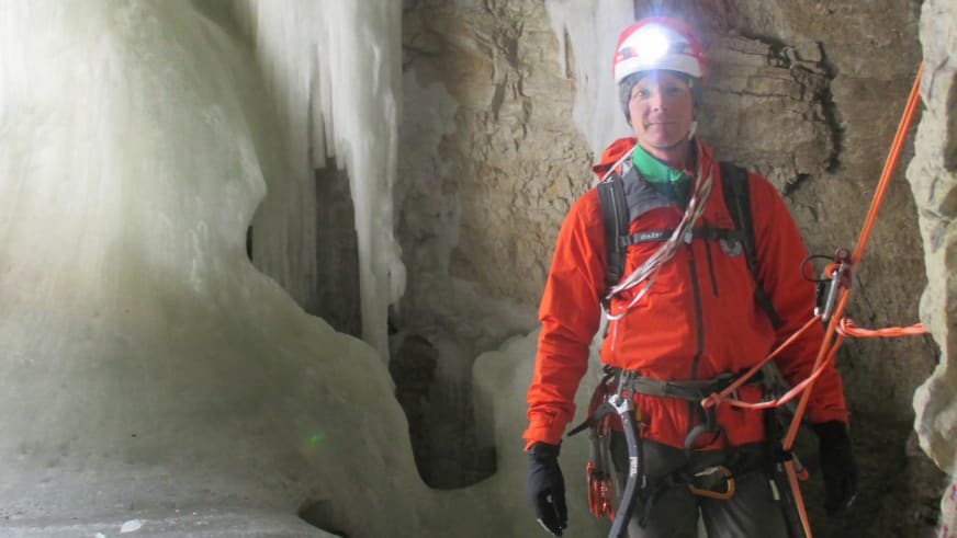 In einer Eishöhle steht Bergführer Thomas Hochrein in oranger Bergausrüstung mit weißem Helm und orangefarbenen Eisgeräten in den Händen.