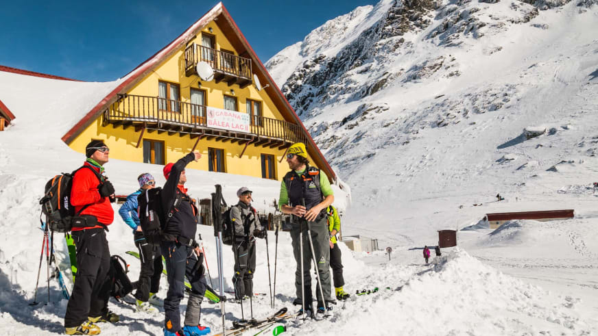 Fünf Skitourengeher stehen vor der gelben Cabana Bâlea Lac auf 2.034 m mit Skiausrüstung im Schnee der Südkarpaten.