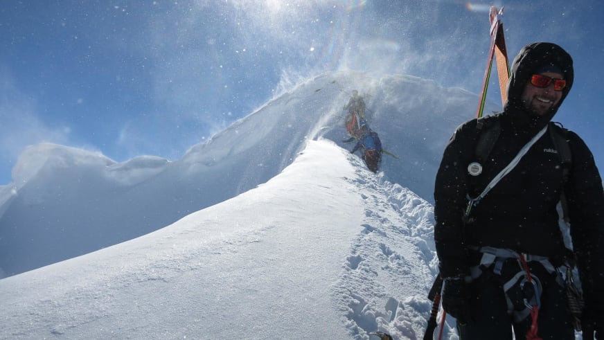 Bei starkem Schneetreiben führt Bergführer Andreas Strasser eine Skitour auf verschneitem Berggrat mit Ski über der Schulter.