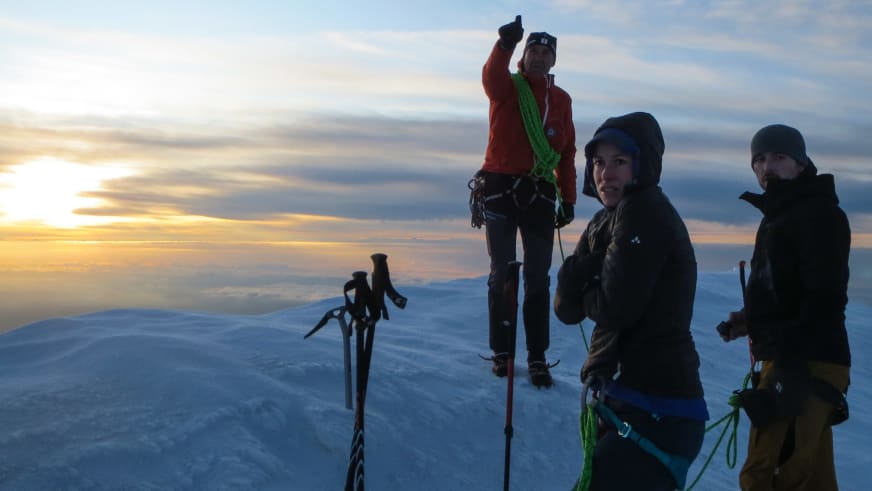 Drei Personen mit Bergführer Hubert Walther stehen bei Sonnenuntergang auf verschneitem Gipfel mit Eispickeln.