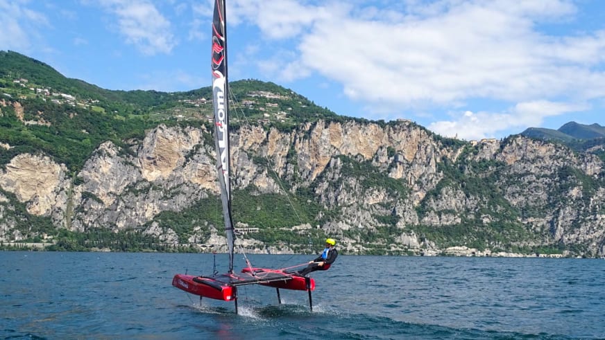 Bergführer Hubert Walther in gelber Kappe steuert roten Katamaran auf Bergsee vor steilen Felswänden.