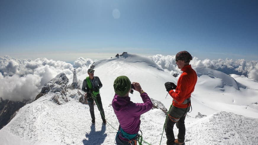 Drei Bergsteiger mit Bergführer Hubert Walther stehen auf verschneitem Gipfel oberhalb der Wolkendecke.
