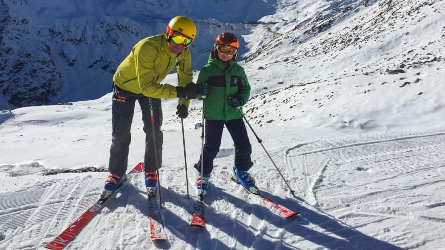 Auf präparierter Piste unterrichtet Bergführer Hubert Walther in gelber Jacke ein Kind im Skifahren.