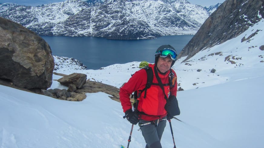 Bergführer Hubert Walther in roter Skijacke steht mit Skistöcken vor tiefblauem Fjord in Nordnorwegen.
