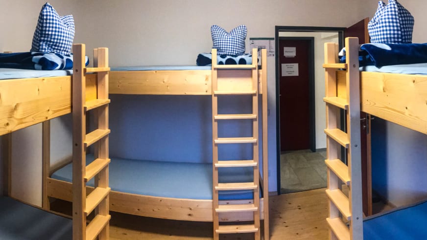 Zimmerlager im Stöhrhaus mit drei Etagenbetten aus Holz und blauer Bettwäsche für Bergwanderer.