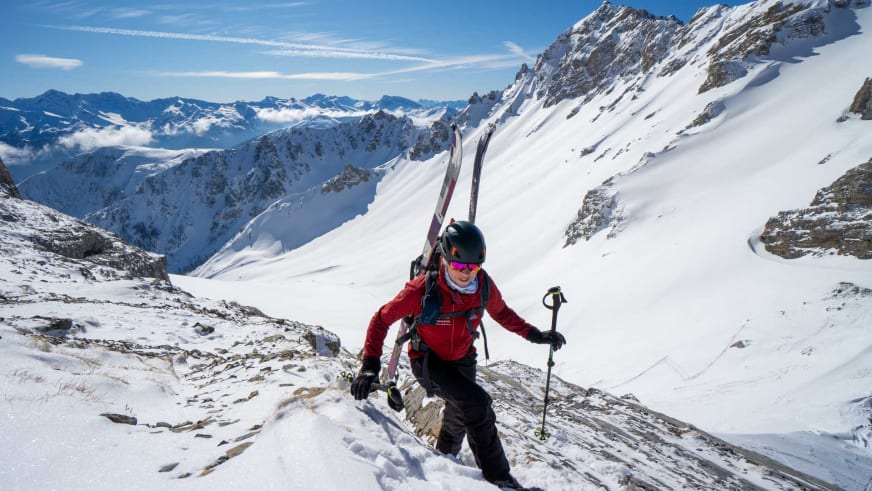 Bergwanderführerin Maria Müller mit Tourenski am Rücken und Skistock steigt über steilen, verschneiten Hang im Hochgebirge auf.