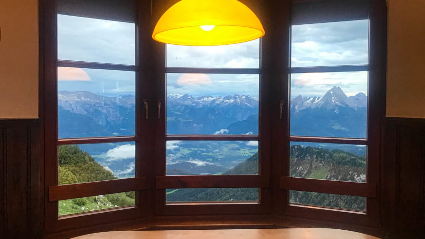 Aufenthaltsraum im Stöhrhaus mit großem Panoramafenster und Blick auf die schneebedeckten Gipfel der Alpen.