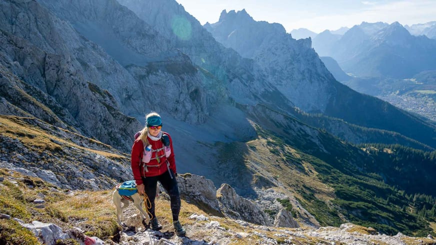 Bergwanderführerin Maria Müller mit gelbem Rucksack steigt über steiles Felsgelände mit Dolomiten-Panorama im Hintergrund.