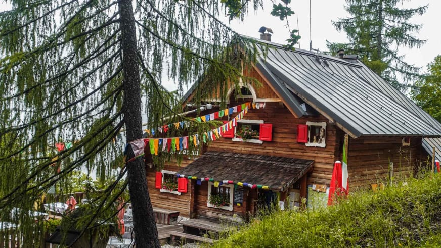 Das Rifugio Luigi Zacchi steht zwischen Fichten mit bunten Gebetsfahnen und roter Fensterläden auf 1.396 m Höhe.