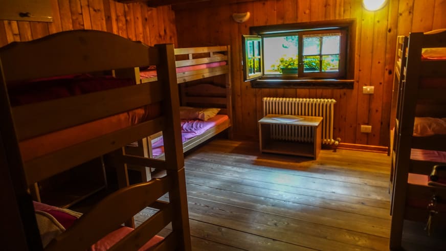 Schlafzimmer im Rifugio Luigi Zacchi mit Etagenbetten aus Holz und traditioneller Holzverkleidung der Wände.