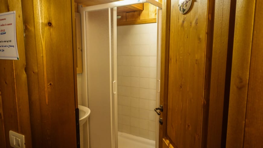 Badezimmer im Rifugio Luigi Zacchi mit weißer Duschkabine und traditioneller Holzverkleidung an den Wänden.