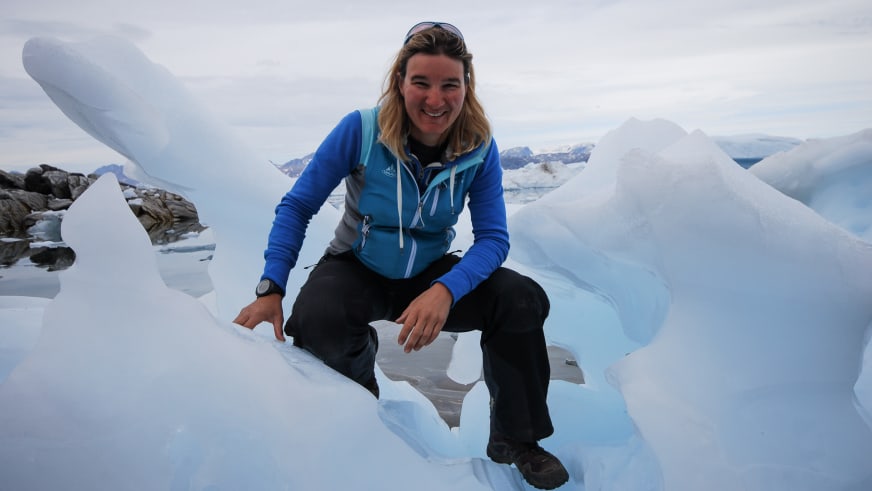 Zwischen großen weißen und bläulich schimmernden Eisblöcken hockt Bergwanderführerin Karin Toni Bigel entspannt und lächelt.