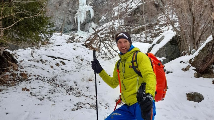 In gelber Softshelljacke steht Bergführer Rolando Varesco mit Wanderstock und Seil in verschneiter Schlucht.