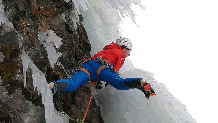 Bergführer Rolando Varesco klettert mit Eispickeln und Steigeisen an einer steilen blauen Eiswand im Winter.