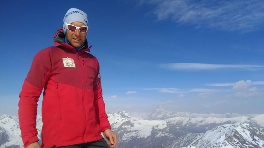 Portrait von Bergführer Rolando Varesco mit weißer Mütze und Gletscherbrille auf einem schneereichen Gipfel.