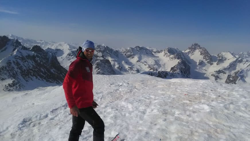 Auf einem schneereichen Gipfel posiert Bergführer Rolando Varesco in roter Jacke für ein Gipfelfoto vor Bergpanorama.