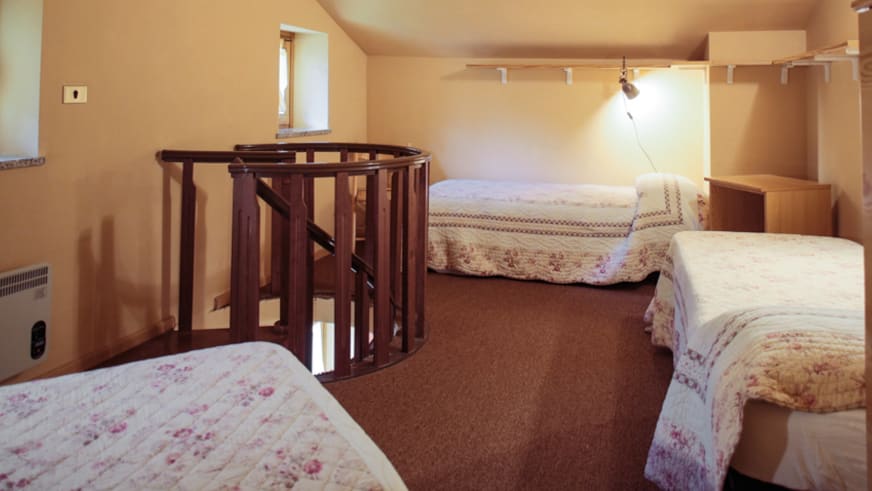 Mehrbettzimmer der Pensione Ceaglio mit vier Einzelbetten, weißer Bettwäsche und Holztreppe zum Obergeschoss.