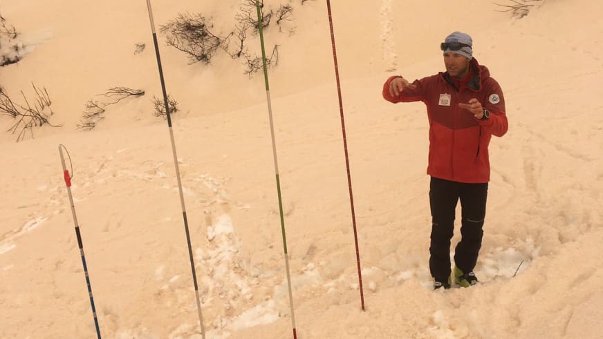 Bergführer Rolando Varesco demonstriert in roter Winterjacke den Umgang mit einer Lawinensonde im Schnee.