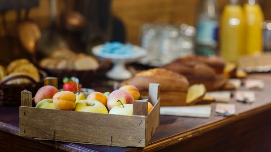 Frühstücksbuffet im Hotel Ceaglio zeigt eine Holzkiste mit Äpfeln und Pfirsichen auf einem Holztisch.