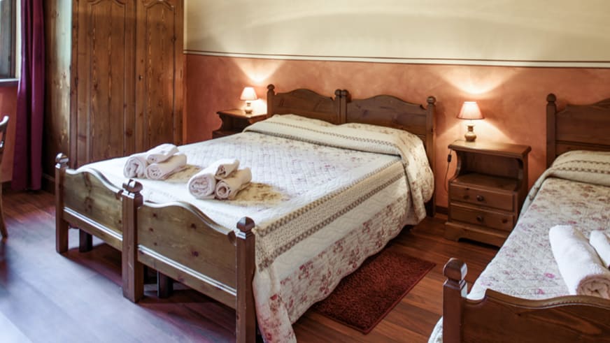 Doppelzimmer der Pensione Ceaglio mit zwei Einzelbetten aus dunklem Holz und alpiner Wandgestaltung.