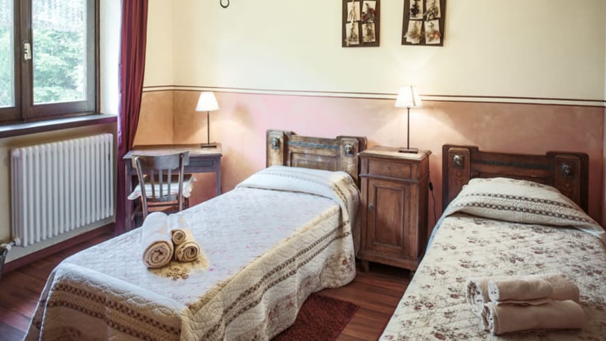 Hotelzimmer in der Pensione Ceaglio mit rustikalen Holzmöbeln, gemusterten Tagesdecken und historischen Fotografien.