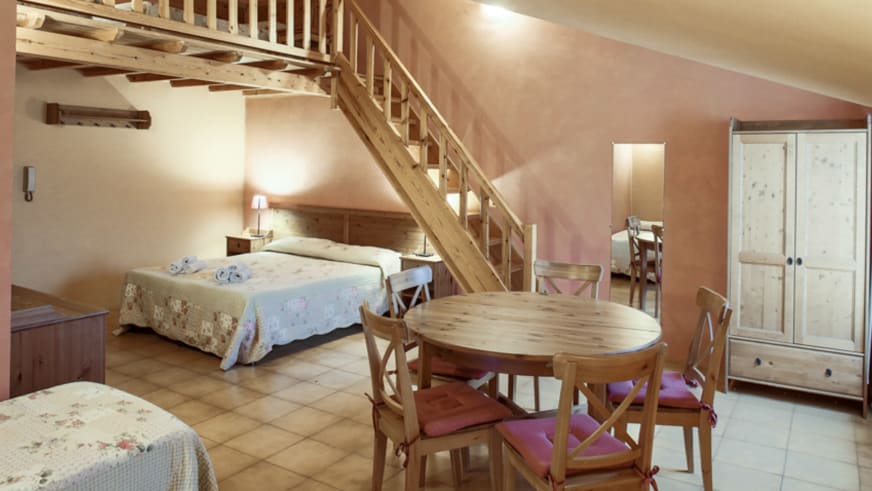 Maisonette-Wohnung in der Pensione Ceaglio zeigt Essbereich mit Holztreppe zum Obergeschoss und rustikale Möbel.