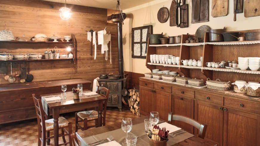 Traditionelle Küche im Hotel Ceaglio zeigt einen gusseisernen Holzofen und Holzvitrine mit weißem Porzellan.