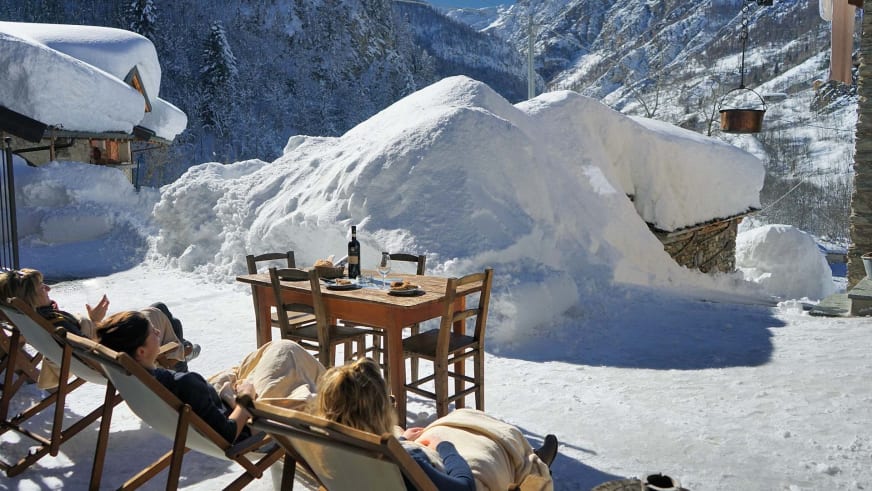 Winterterrasse der Pensione Ceaglio mit Liegestühlen, Whirlpool und Bergblick auf die schneebedeckten Hänge des Valle Maira.